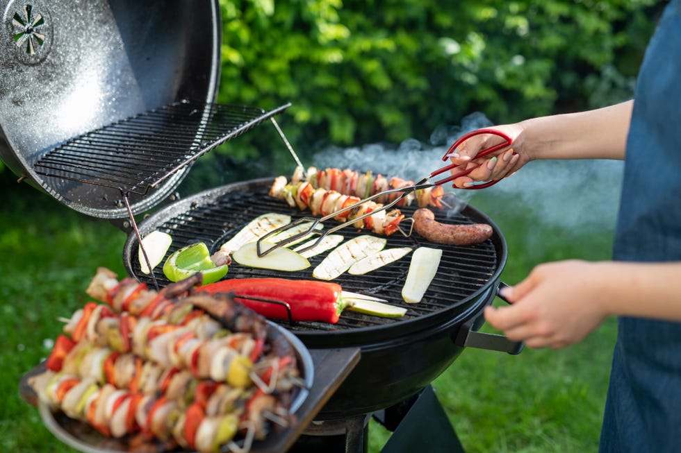 woman with grill tongs turns food on a hot grill at the back yard.
