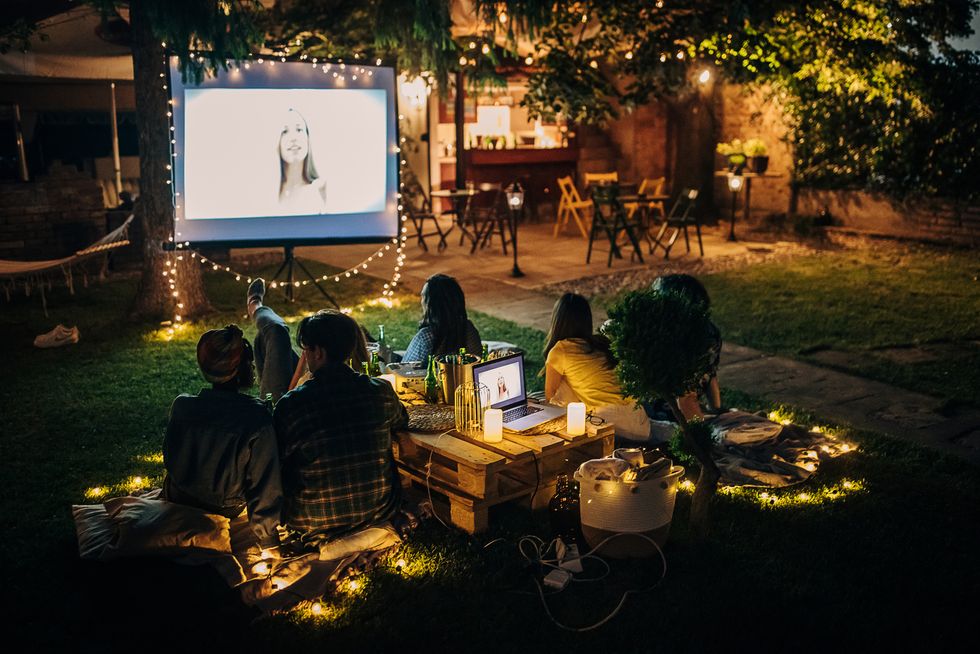 friends sitting on blankets watching movie on the video projector in the backyard with fairy lights and candles
