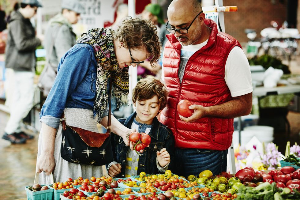 mom, dad and young boy examining tomatoes while shopping at farmers market