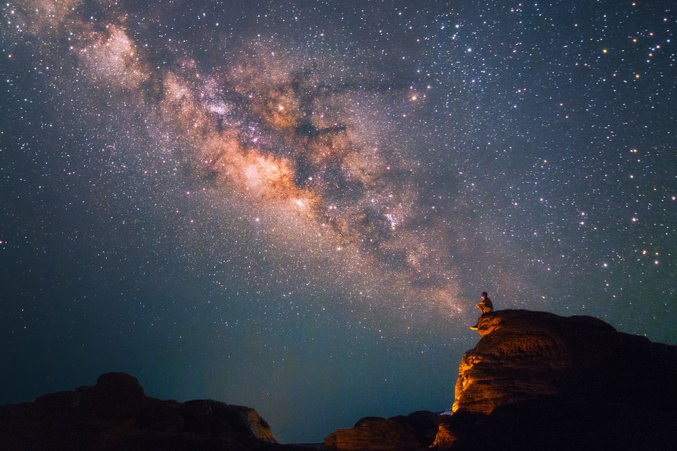 silhouette man sitting on the top a massive rock looking at the milky way
