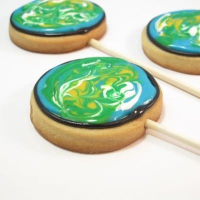 three cookies on a stick that are all decorated to look like earth in blue, green, white and yellow