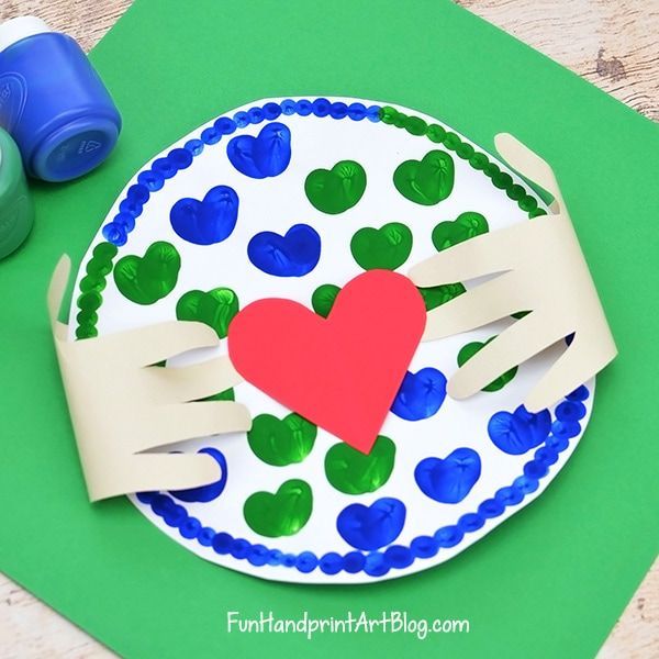 cut out hands holding a round piece of paper painted with blue and green hearts with a red heart in the middle