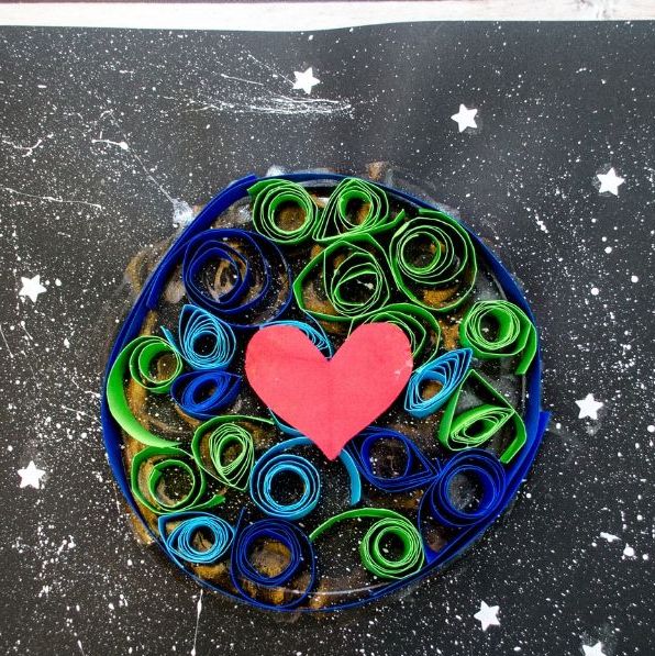 earth made from blue and green quilled paper seen from above against a background of black paper with stars there is a red heart on the earth