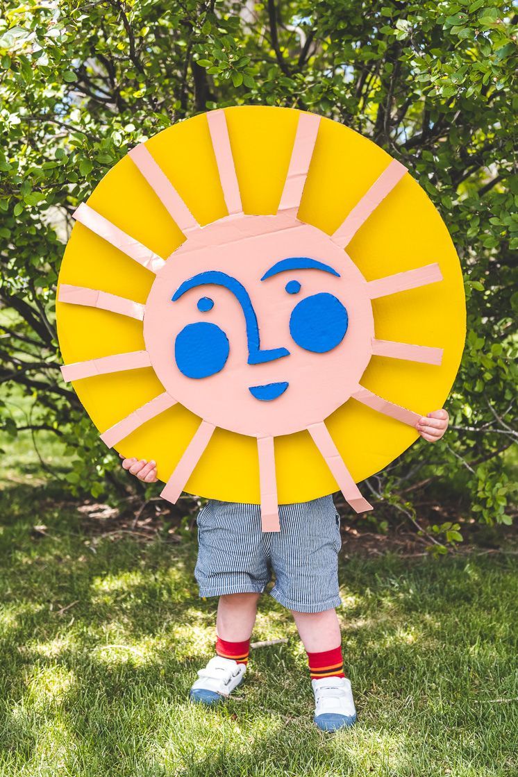 child holding and covering his upper body with a sun with a blue smiling face made out of cardboard
