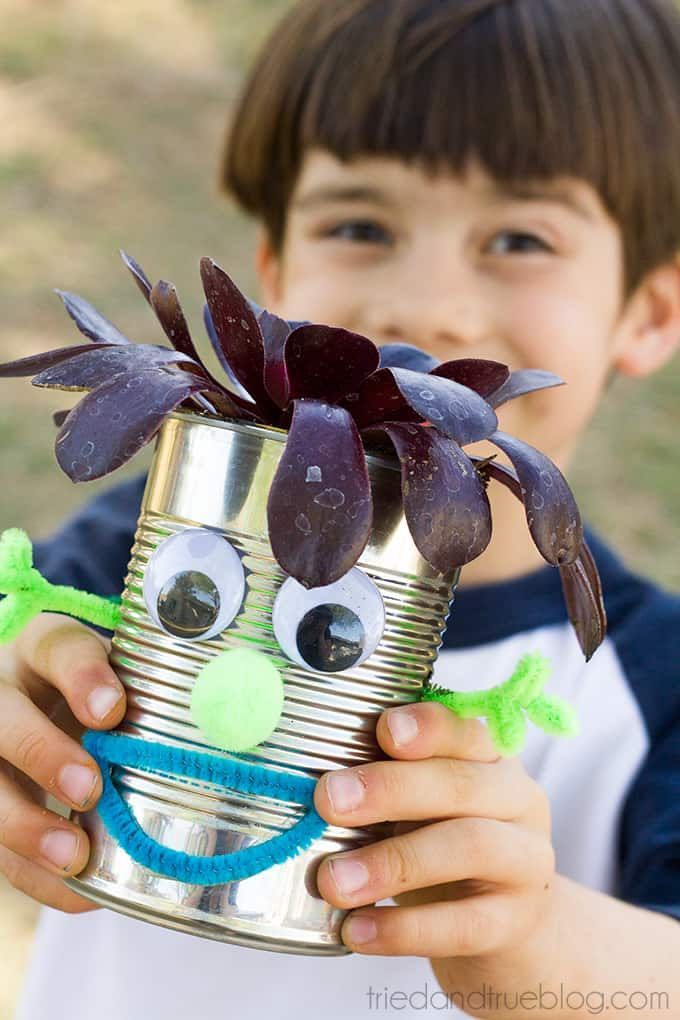 child holding out a tin can with googly eyes and a pipe cleaner mouth and arms on it