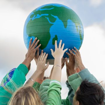 group of teenagers holding up a blue and green globe of the earth against the sky