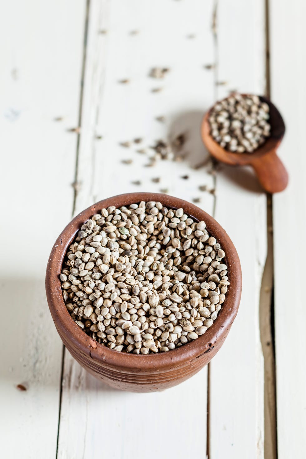 Earthenware dish and wooden spoon of organic hemp seed, Cannabis sativa, on white wood