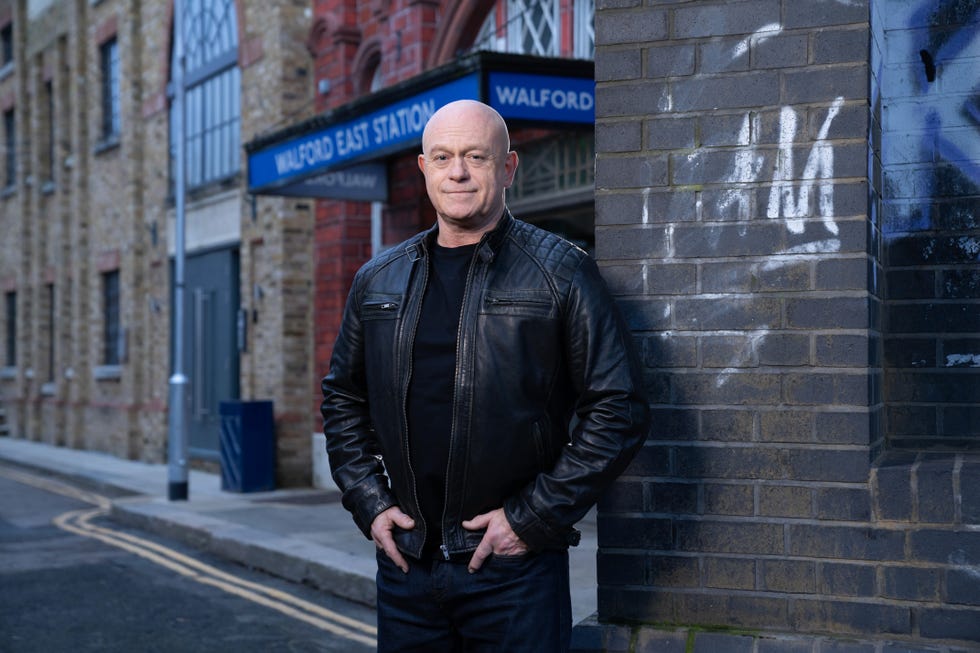 eastenders character grant mitchell smiles as he stands in front of walford east tube station