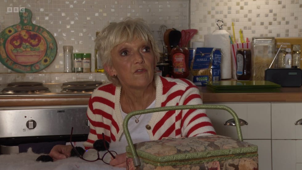 eastenders' jean slater sitting in the kitchen wearing a striped sweater, with various kitchen items around