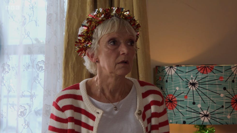 eastenders jean slater wearing a tinsel headband and a striped cardigan