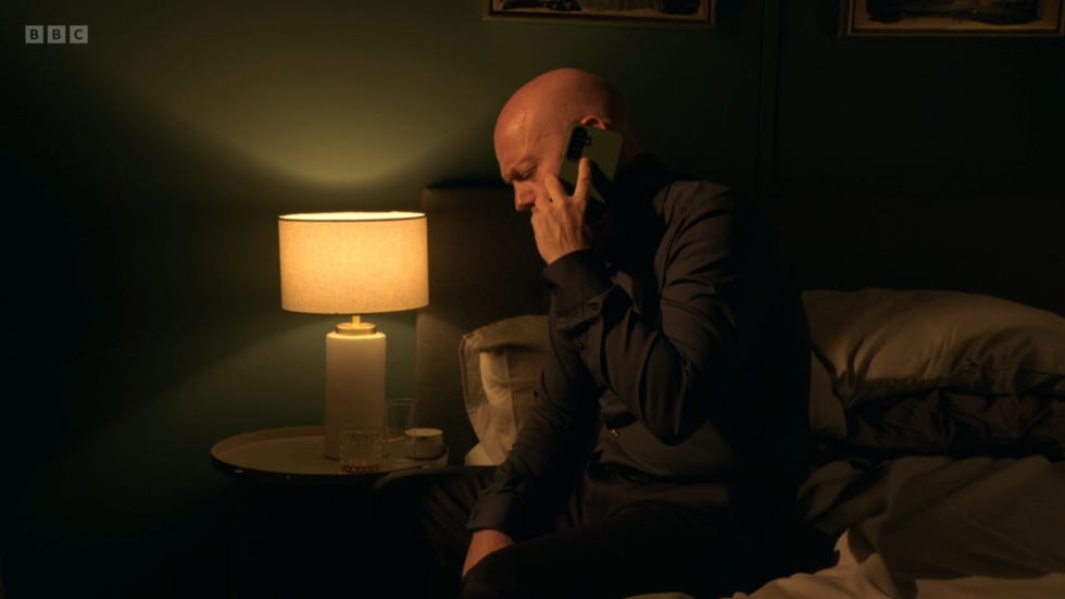 eastenders max branning holding a phone in a dimly lit hotel room