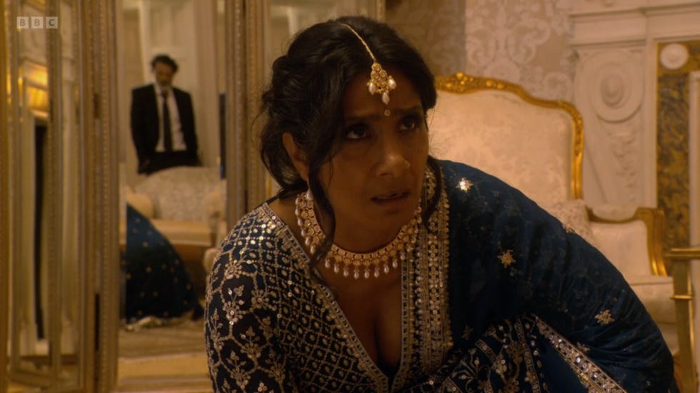 eastenders suki and nish, suki looks terrified in her traditional wedding dress, with nish in the doorway behind her