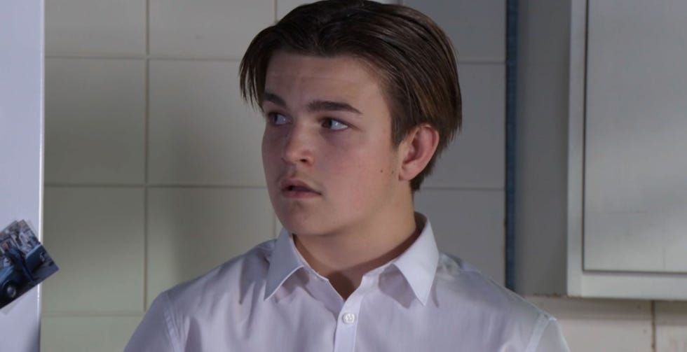 eastenders character tommy moon stands in the kitchen and looks worried as he's questioned about his behaviour