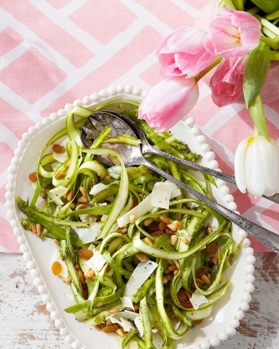 shaved asparagus salad in a white serving bowl with utensils
