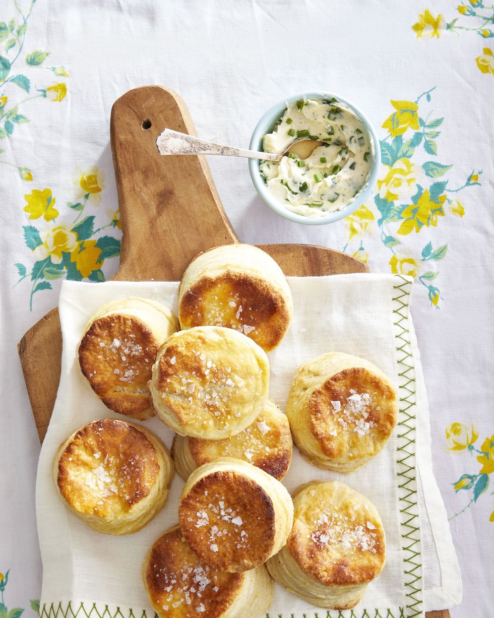 cornmeal butter biscuits piled on a wooden serving board with a small bowl of chive butter on the side