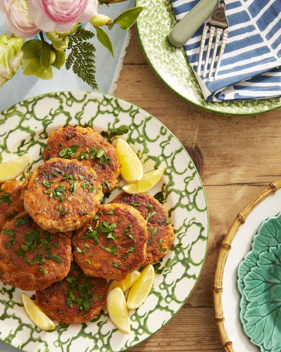 salmon patties arranged on a serving plate with lemon wedges and sprinkled with chopped fresh herbs