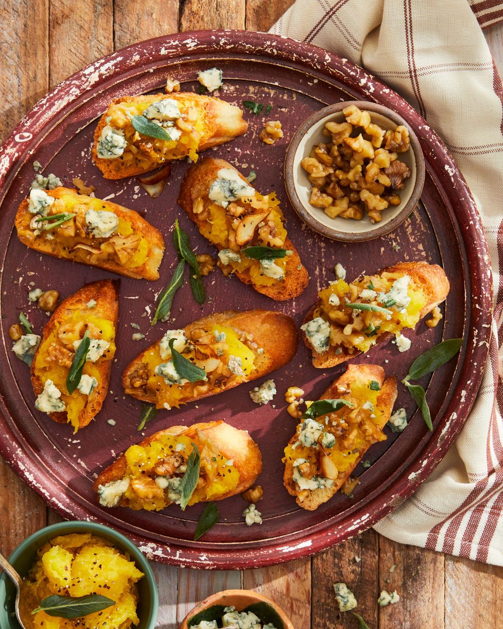 smashed acorn squash and garlicky walnut crostini on a dark red plate with small bowls of toppings on the side