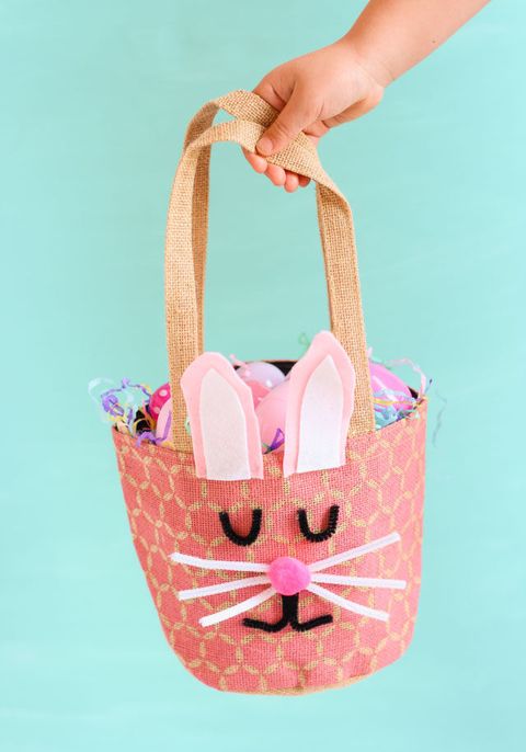 easter basket ideas, hand holding a diy bunny basket with a pom pom nose and pipe cleaner whiskers