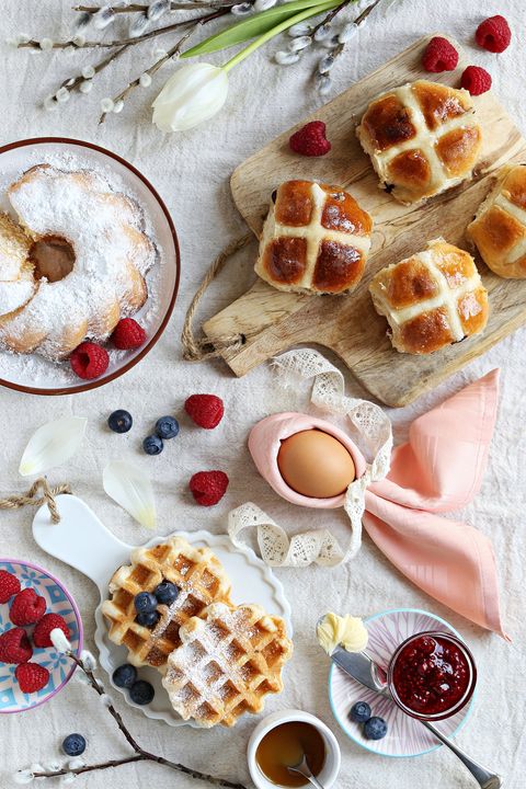easter festive dessert table with hot cross buns, cakes, waffles and pancakes overhead view