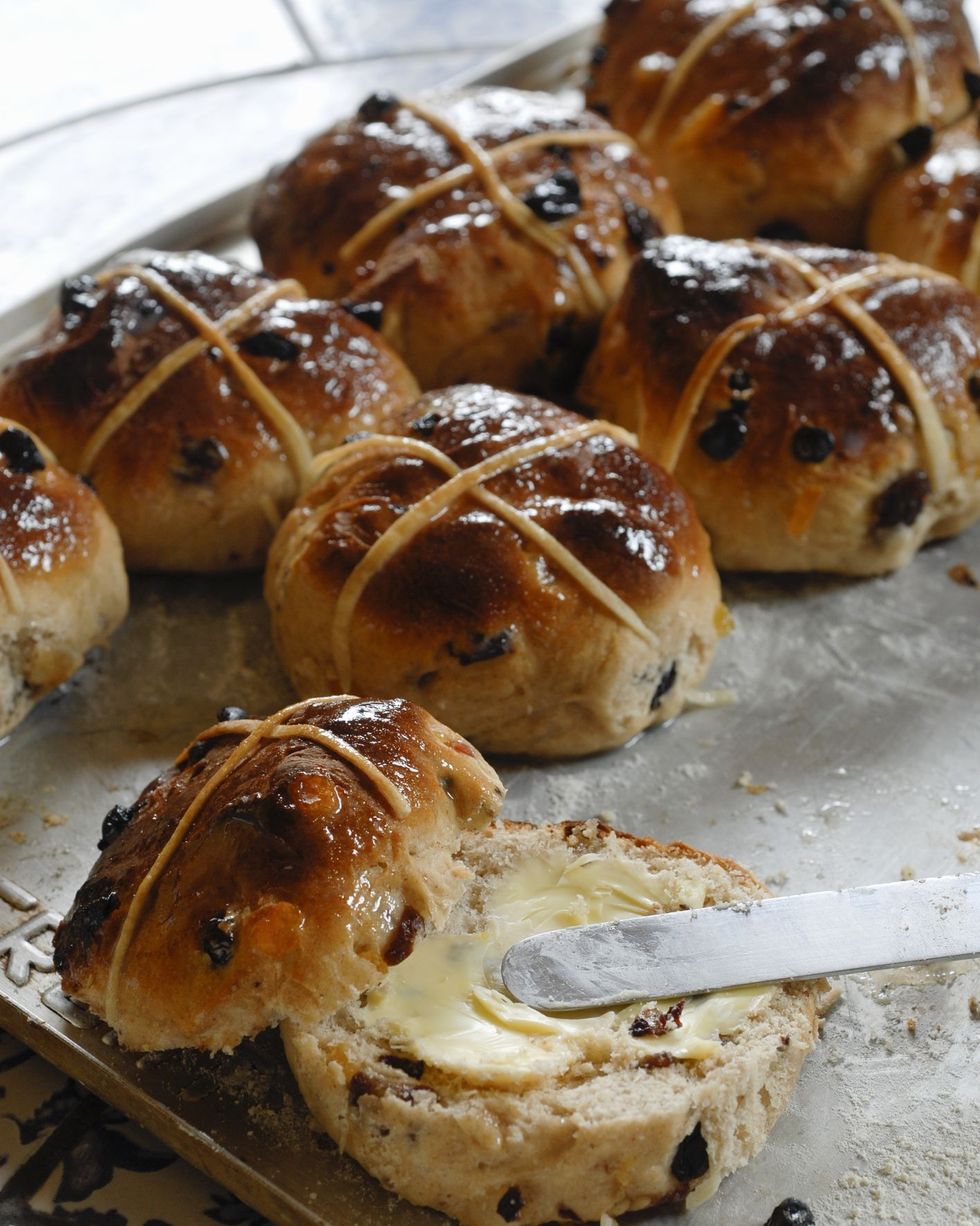 hot cross buns on a sheet pan with one cut in half and butter spread on one side