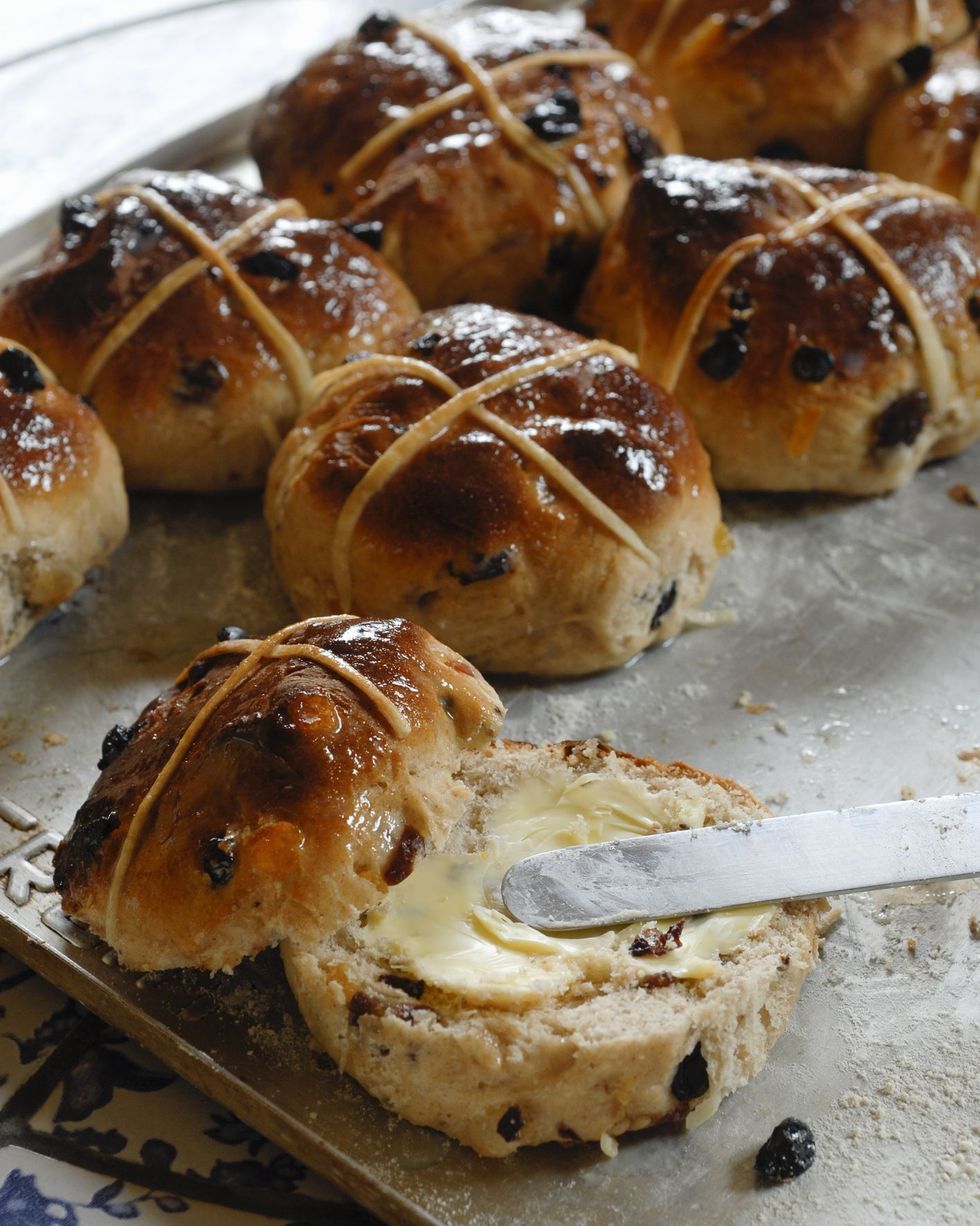 hot cross buns on a sheet pan with one cut in half and butter spread on one side