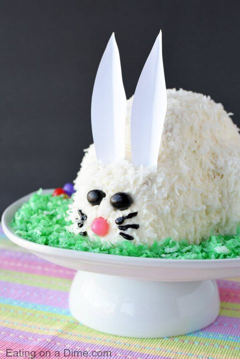 easy easter bunny cake covered in shredded coconut and decorated with candy for the face and paper ears