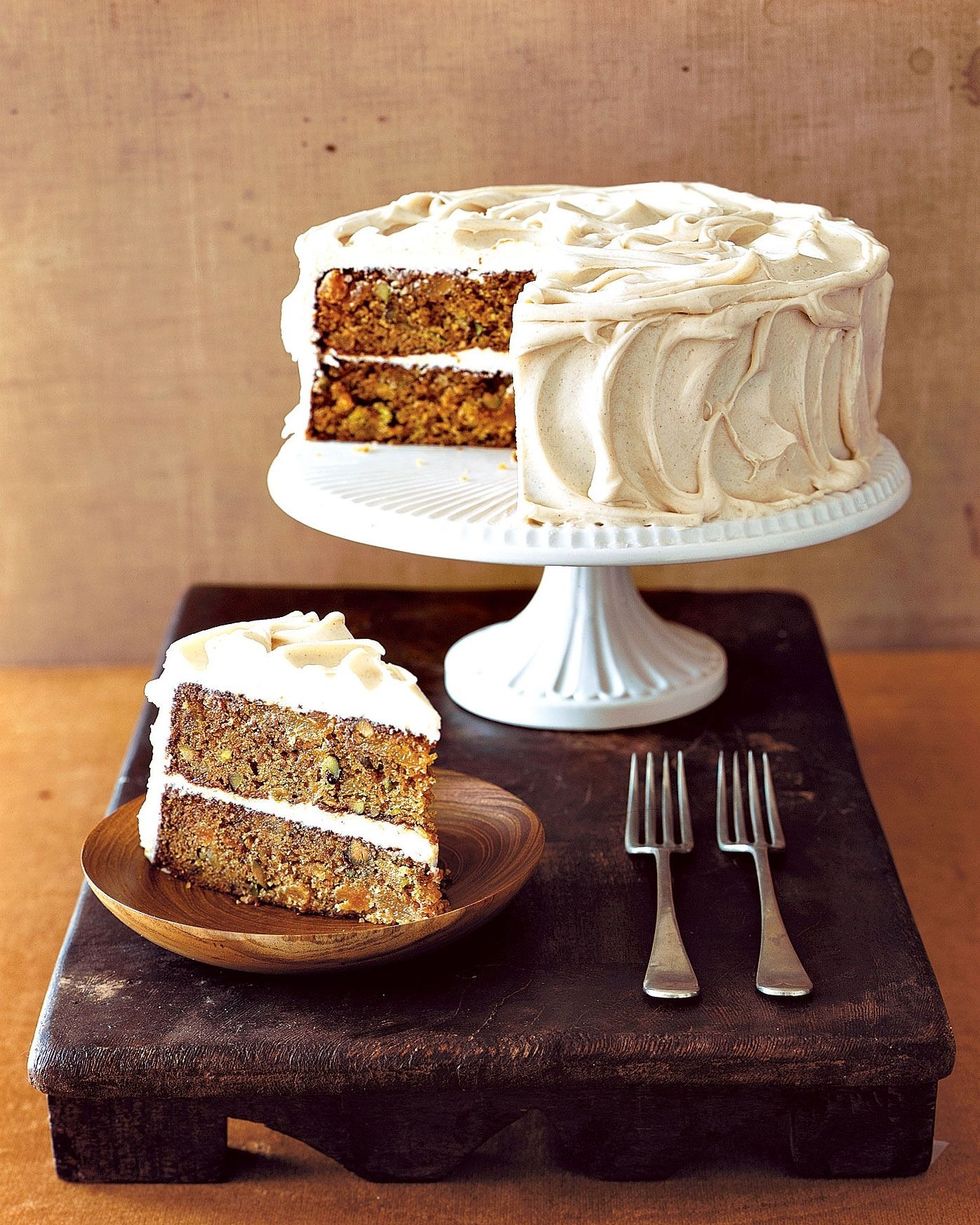 carrot pistachio cake on a white cake stand with a slice on a wooden plate with forks