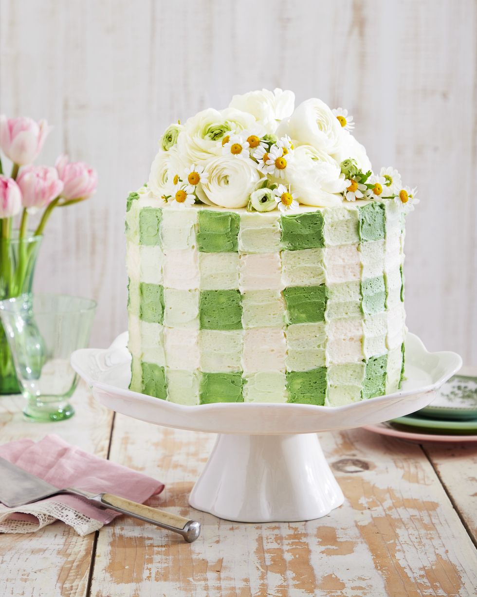 coconut cream gingham cake with a light green gingham patterned frosting on a white cake stand and topped with fresh flowers