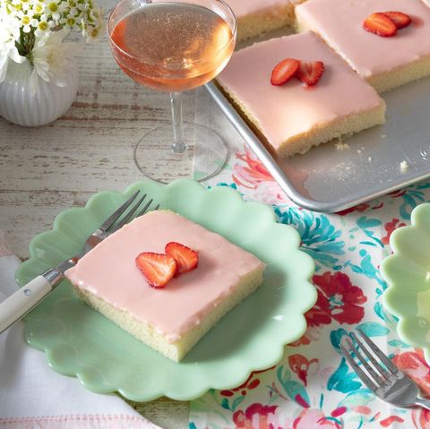 strawberries and rose sheet cake slice on green plate in front with glass of wine