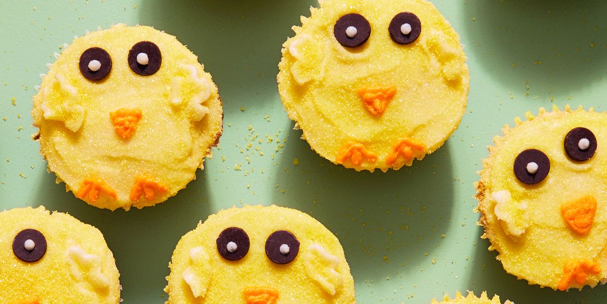 cupcakes with yellow frosting and sanding sugar decorated to look like easter chicks with chocolate chip eyes and an orange frosting beak and feet