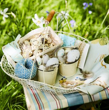 a wire basket filled with eggs, feathers and twine on a fabric stool