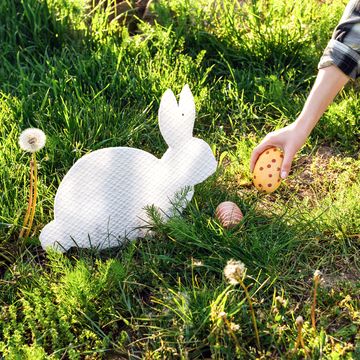person picking up an easter egg in a yard with bunny decorations