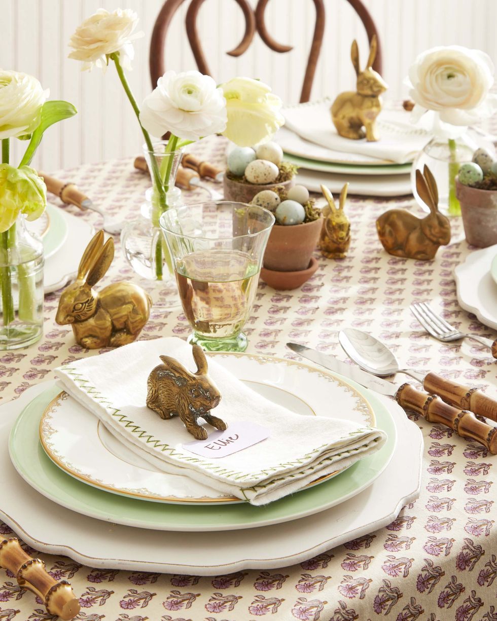 set table with brass bunny on top of a stack of plates and a white linen with green detailing