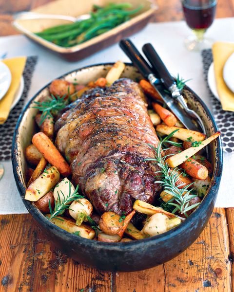 butterflied leg of lamb with root vegetables in a large stone serving bowl with utensils for serving