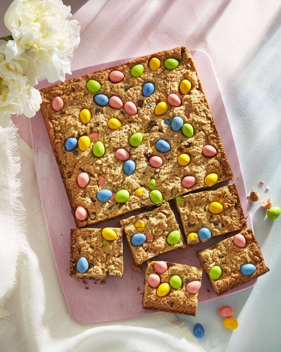 peanut butter and candy egg blondies on a light pink serving board with some cut into squares