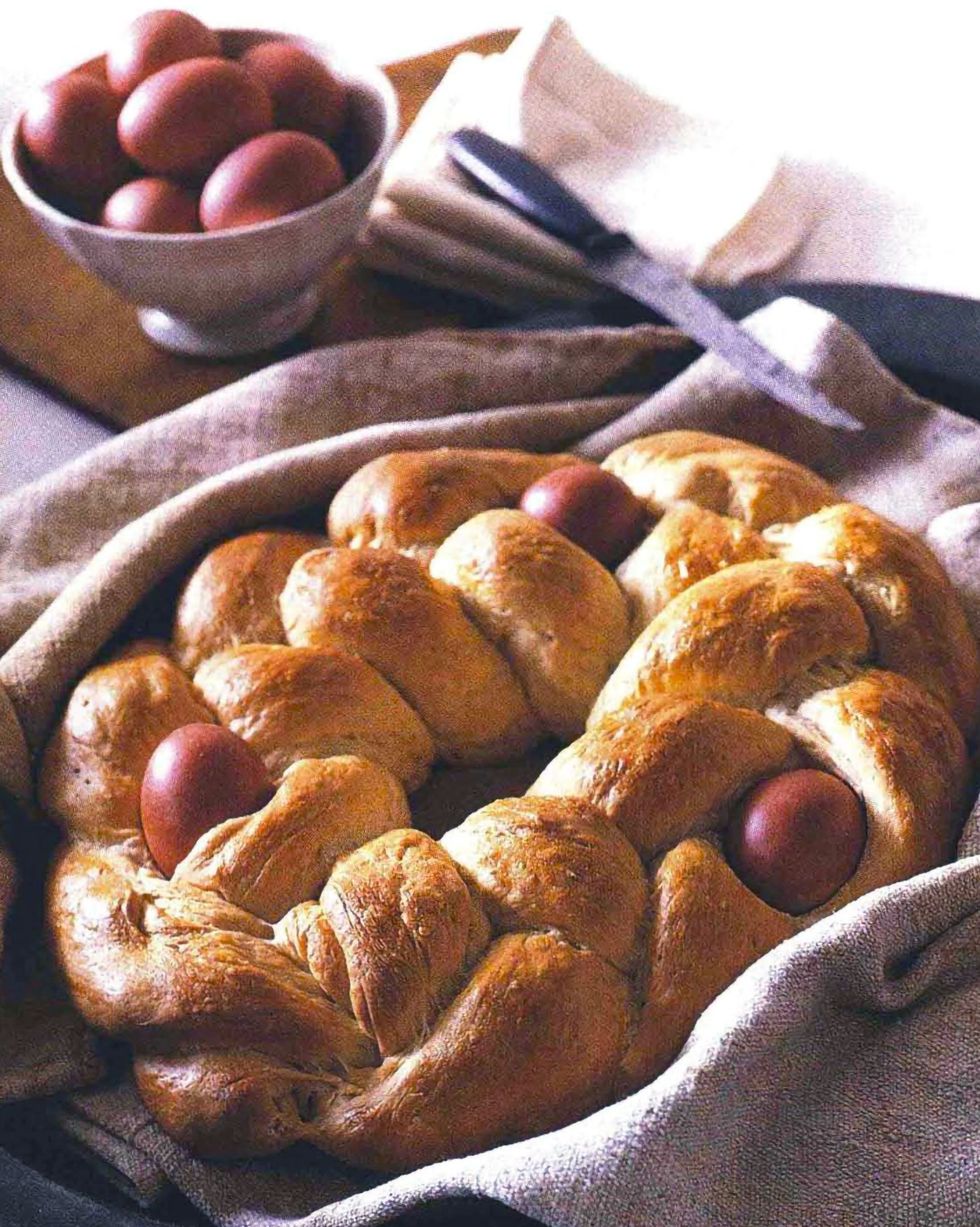 braided easter bread with three dyed eggs baked in on a linen kitchen towel