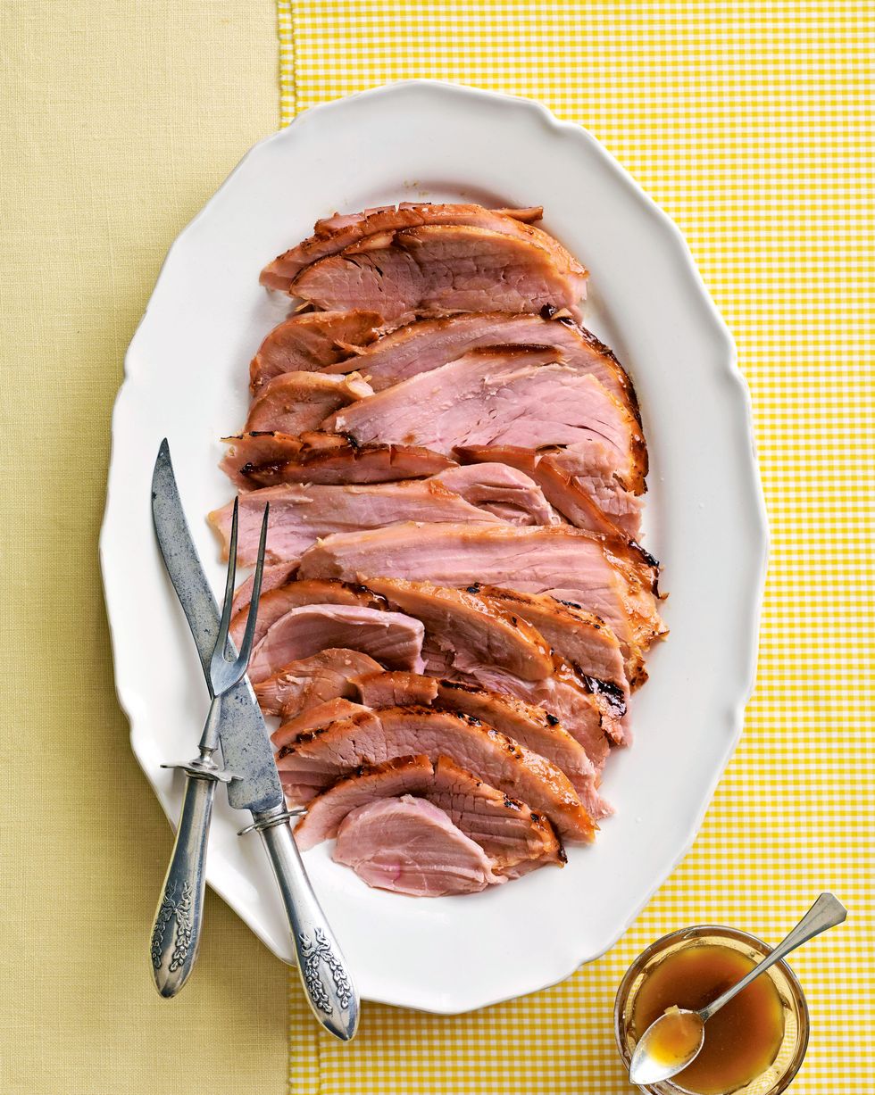 pineapple glazed ham sliced and arranged on a white oval serving plate with utensils