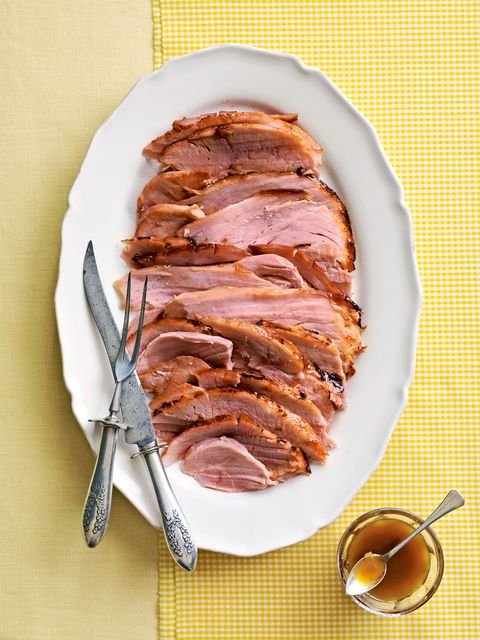 pineapple glazed ham sliced and arranged on a white oval serving plate with utensils