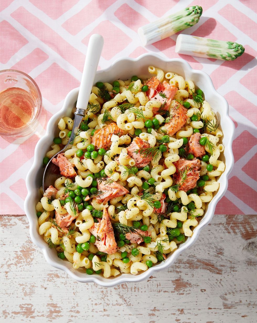 spring pasta with salmon peas and dill in a white scalloped oval serving bowl with a spoon