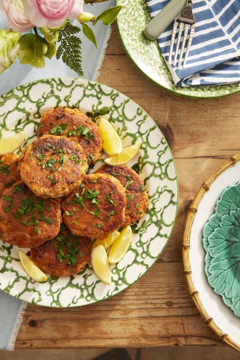 salmon patties stacked on a green and white patterned plate with lemon wedges and sprinkled with herbs