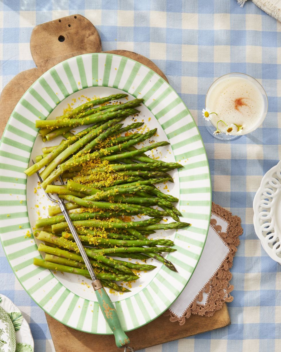 salt cured egg yolks grated over steamed asparagus on an oval serving plate with a serving utensil