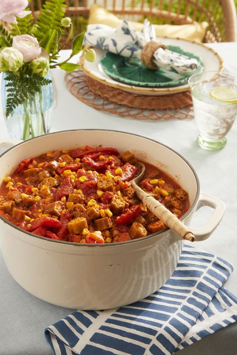 stewed okra and tomatoes in a large cream colored dutch oven with a wooden spoon for serving