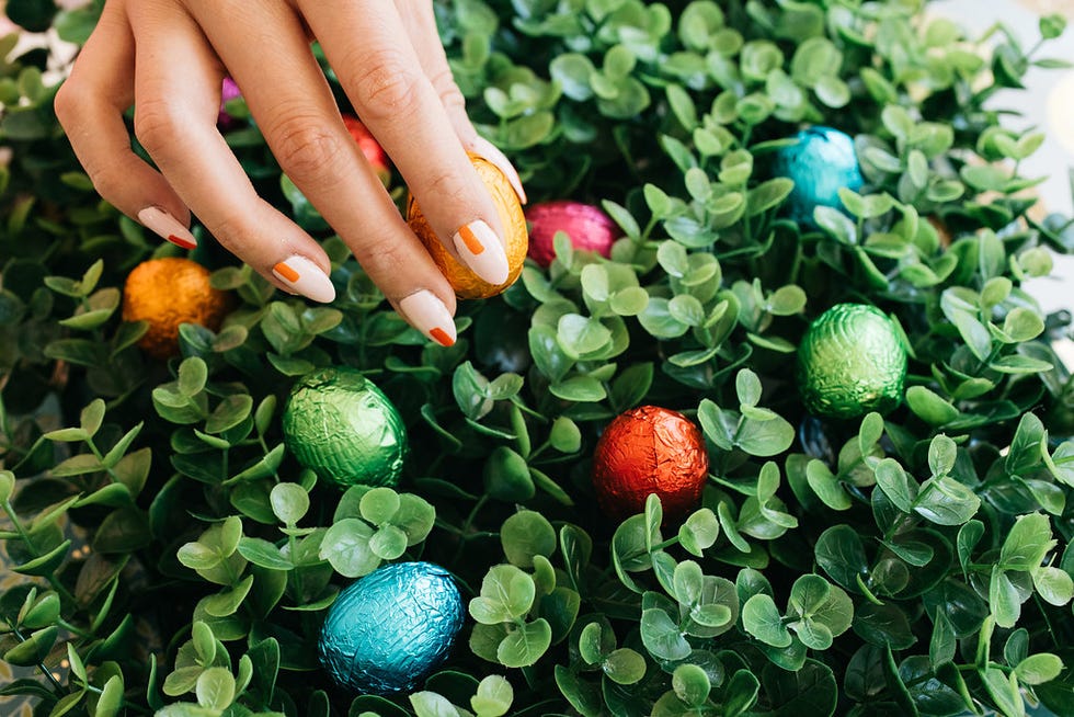 a person with painted fingernails in peach and orange picking up some easter candy