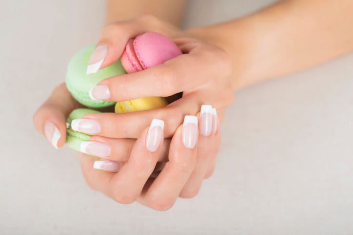 girl holding colorful macarons in hands with french manicure