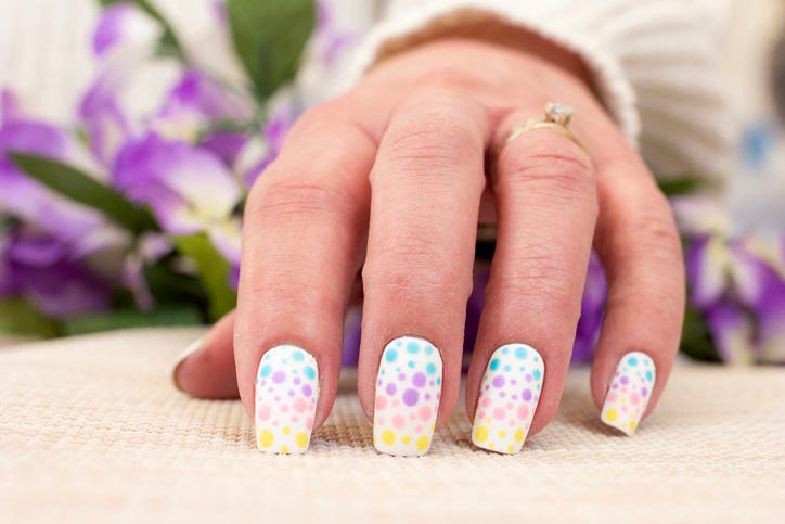 a womans manicure in white with painted on dots in different pastel colors