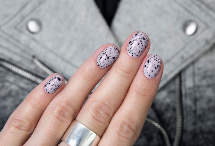 a womans manicure with a grayish purple base and black splatters that look like speckled eggs