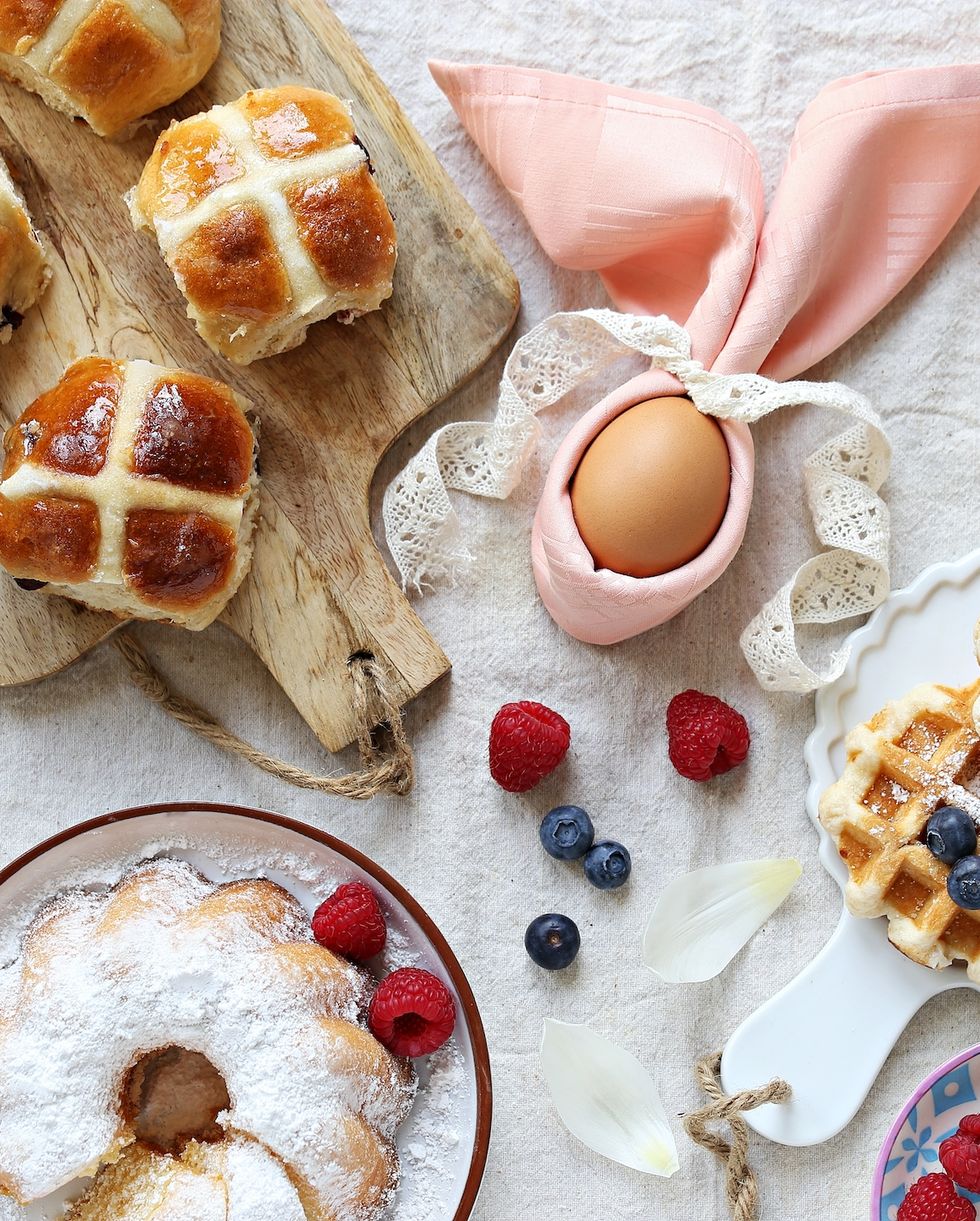 easter festive dessert table with hot cross buns, cakes, waffles and pancakes overhead view