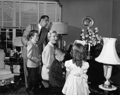 black and white photo of family carrying out easter tradition of singing songs around the piano