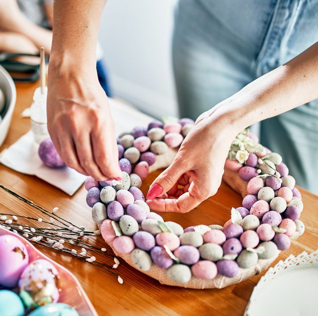 close up of women's hands making a wreath of eggs for easter top view