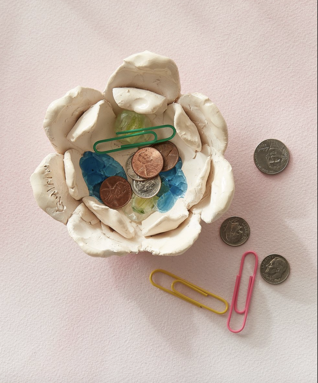 a small bowl made from oven bake clay filled with pennie and paperclips on a pink surface